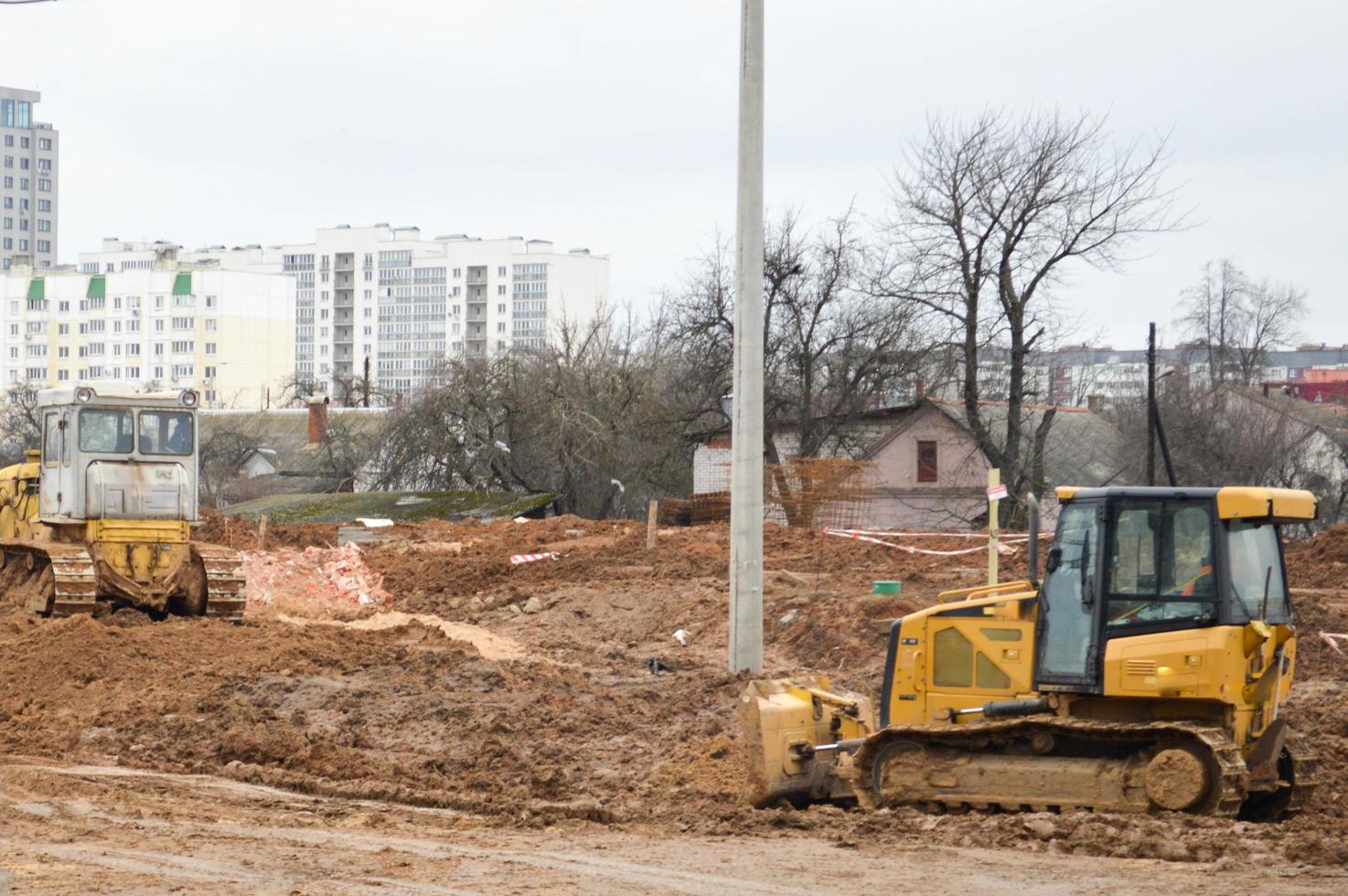 Viele leistungsstarke industrielle schwere spezialisierte Baumaschinen von Traktorbaggern und Bulldozern führen Straßenreparaturen während des Baus eines neuen Mikrobezirks in einer Großstadt durch foto