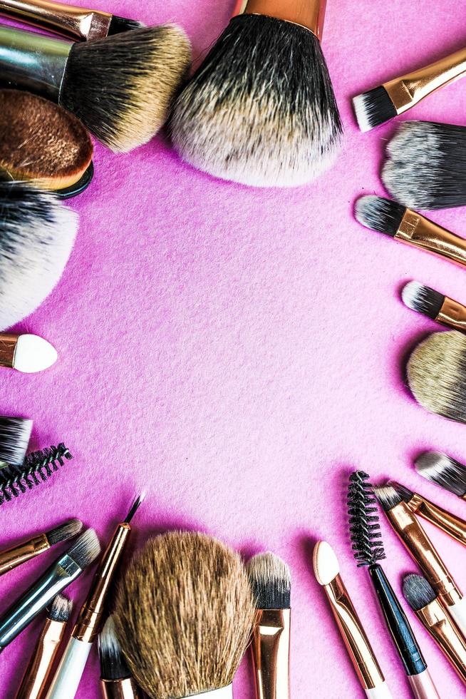 Ein Rahmen aus einer Reihe schöner, unterschiedlicher weicher Make-up-Pinsel aus natürlichen Flusen, um Schönheit ins Visier zu nehmen und eine tonale Basis in einem Ständer aufzutragen und Platz auf einem rosa, violetten Hintergrund zu kopieren foto