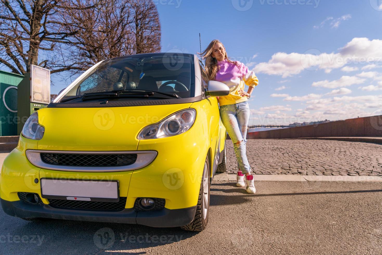 Schöne Frau, die an einem sonnigen Tag in der Nähe eines gelben Autos steht foto