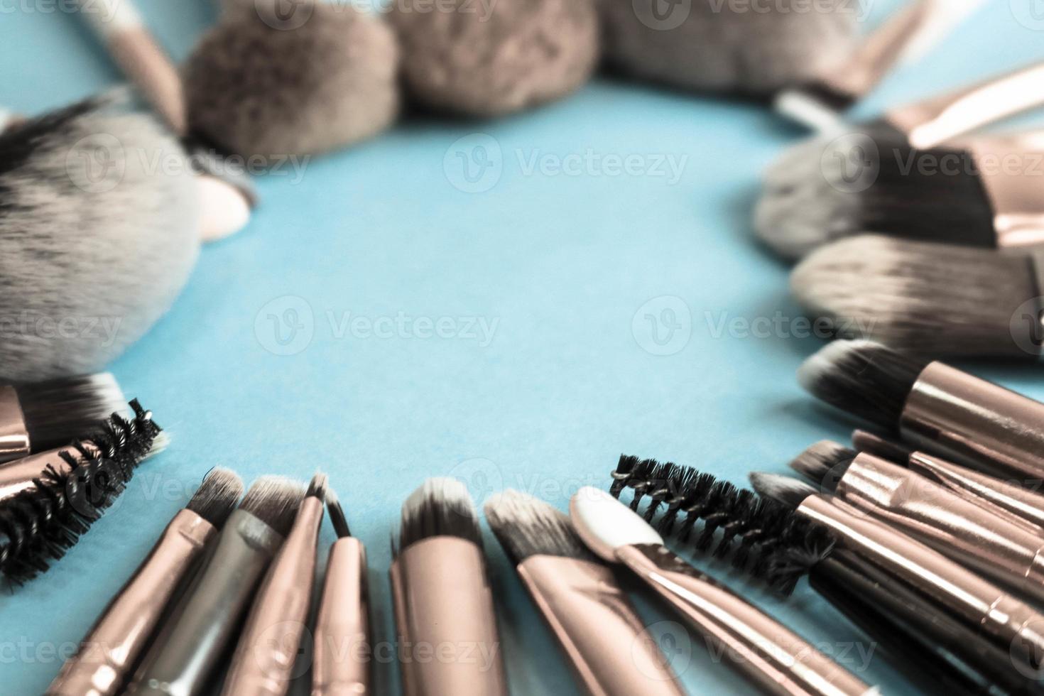 Ein Rahmen aus einer Reihe schöner, unterschiedlicher weicher Make-up-Pinsel aus natürlichen Flusen, um die Schönheit zu erreichen und eine tonale Grundlage in einem Ständer aufzutragen und auf blauem Hintergrund zu kopieren foto