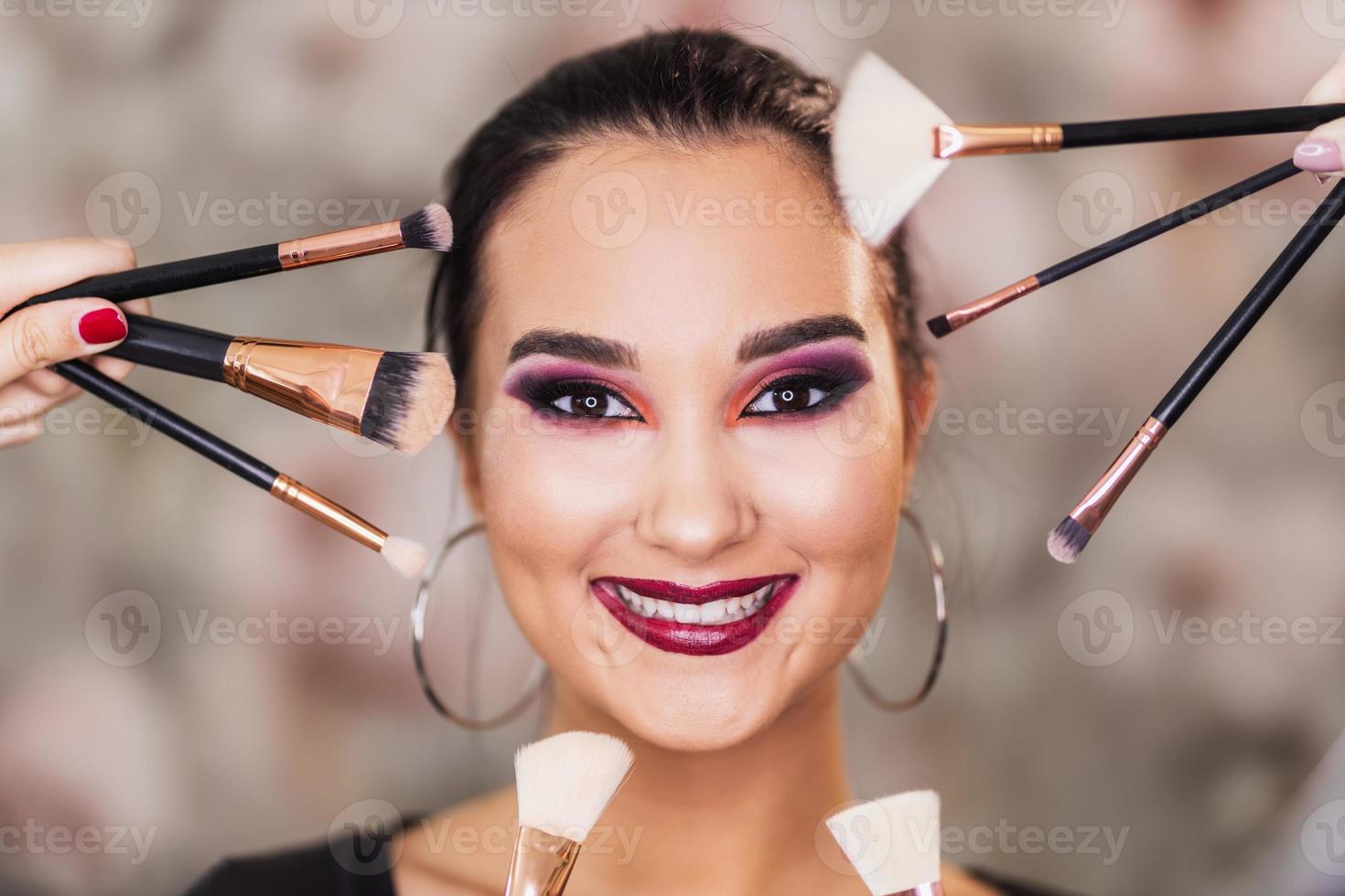 süße Frau mit schönem Make-up, umgeben von Make-up-Pinseln foto