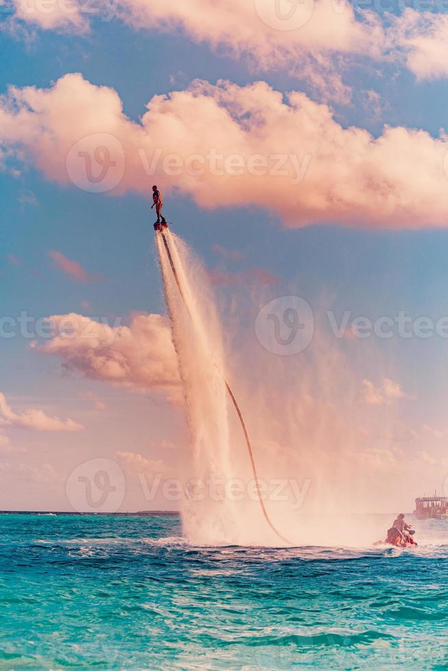 Insel Sonnenuntergang. professioneller Fly-Board-Fahrer, der Backflip mit tropischem Resort-Insel-Hintergrund macht. sonnenuntergangsport und sommeraktivitätshintergrund, lustiger wassersport foto