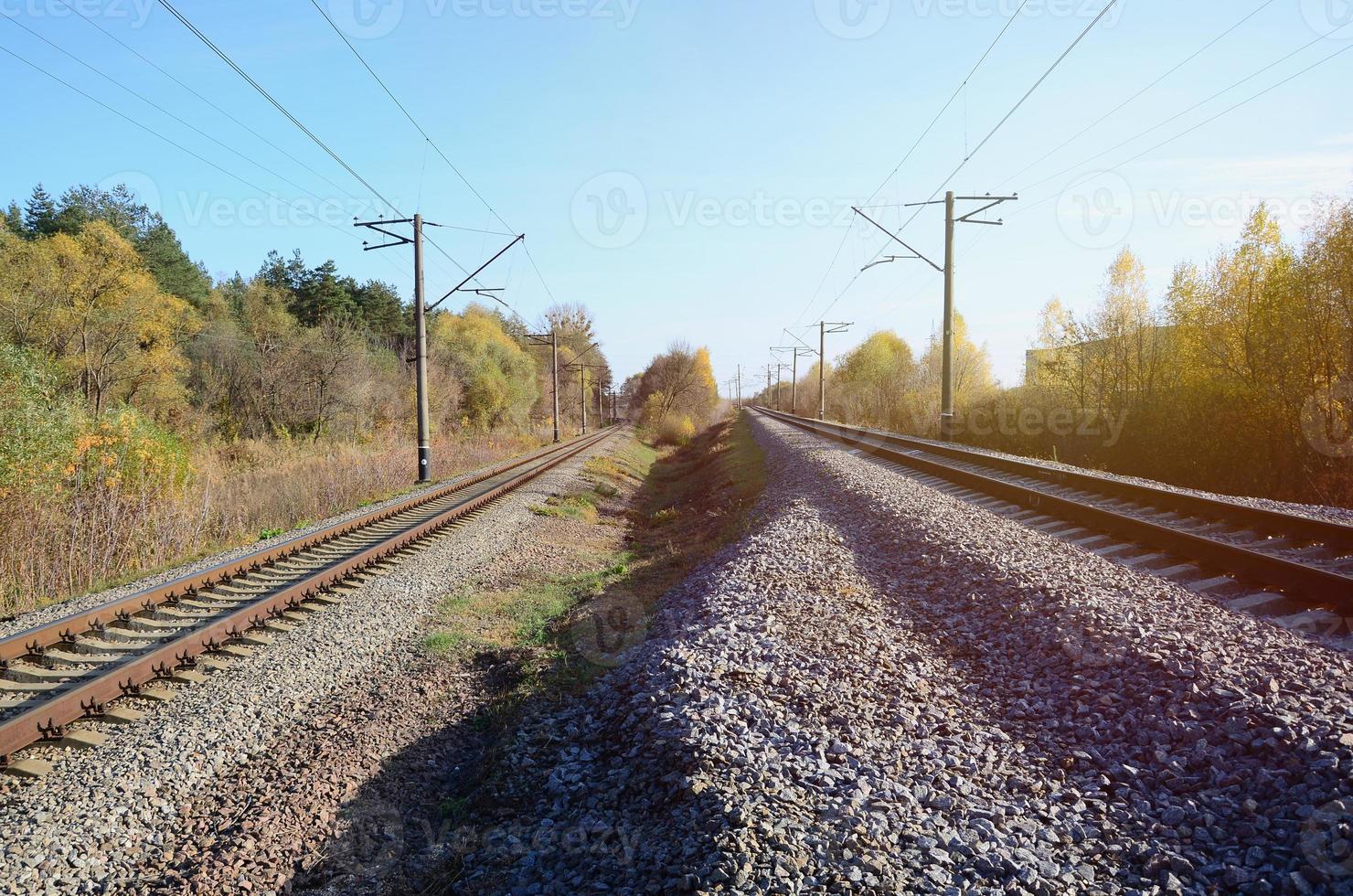 herbstliche Industrielandschaft. Eisenbahn, die sich zwischen grünen und gelben Herbstbäumen in die Ferne zurückzieht foto