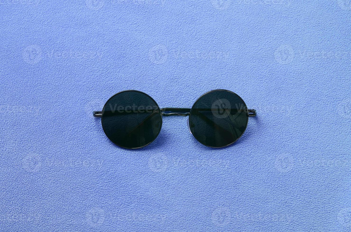 Eine stilvolle schwarze Sonnenbrille mit runden Gläsern liegt auf einer Decke aus weichem und flauschigem hellblauem Fleecestoff. modisches Hintergrundbild in weiblichen Farben foto