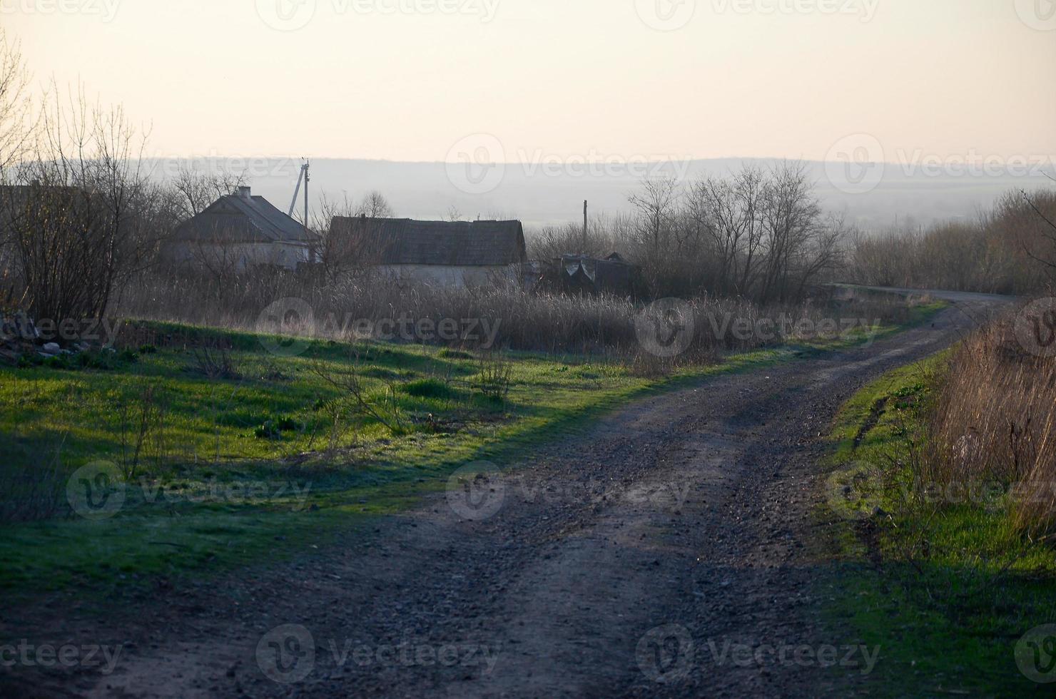 Morgendämmerung im Dorf. Asphaltstraße, die zwischen den Feldern weit in die Ferne geht foto