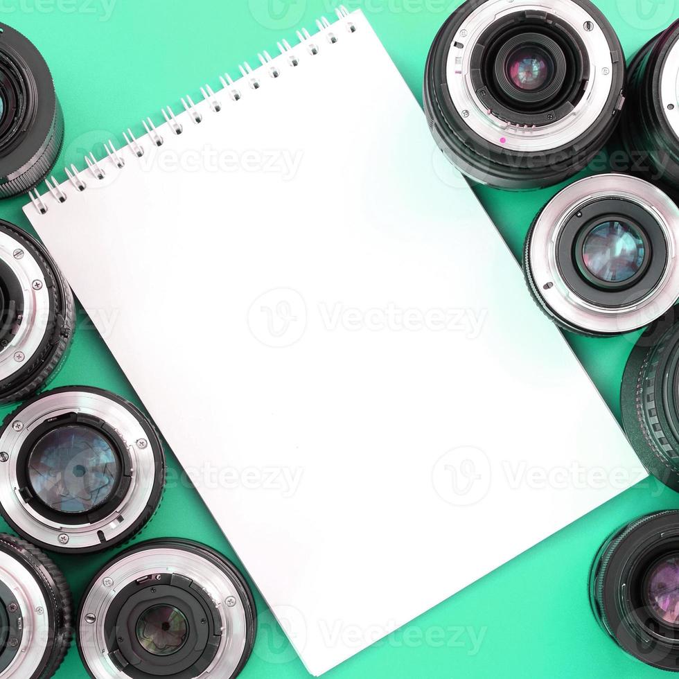Mehrere Fotoobjektive und ein weißes Notizbuch liegen auf einem helltürkisfarbenen Hintergrund. Platz kopieren foto