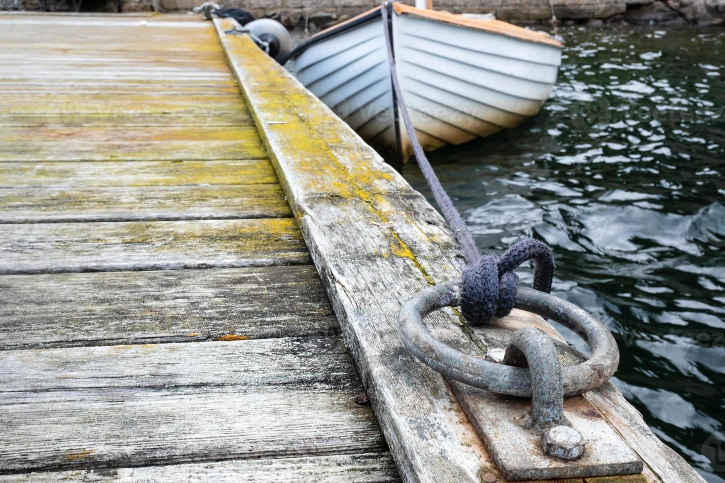 eiserner Festmacherring an einem alten Holzsteg, im Hintergrund ist ein Segelboot verknotet. foto