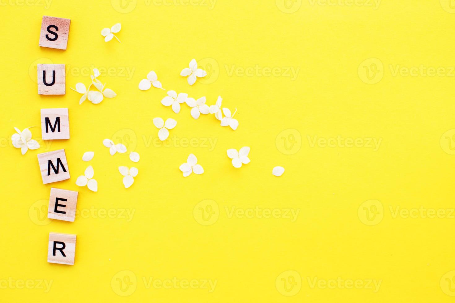 Wort Sommer geschrieben von Holzwürfeln mit Buchstaben auf gelbem Hintergrund mit Blütenblättern einer Hortensie foto