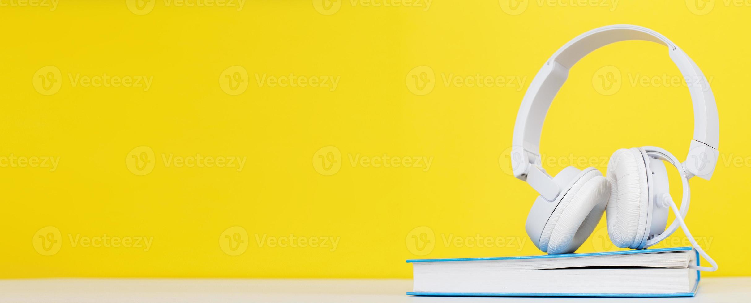 Hörbuchkonzept mit modernen weißen Kopfhörern und gebundenem Buch auf gelbem Hintergrund. ein Buch hören. foto