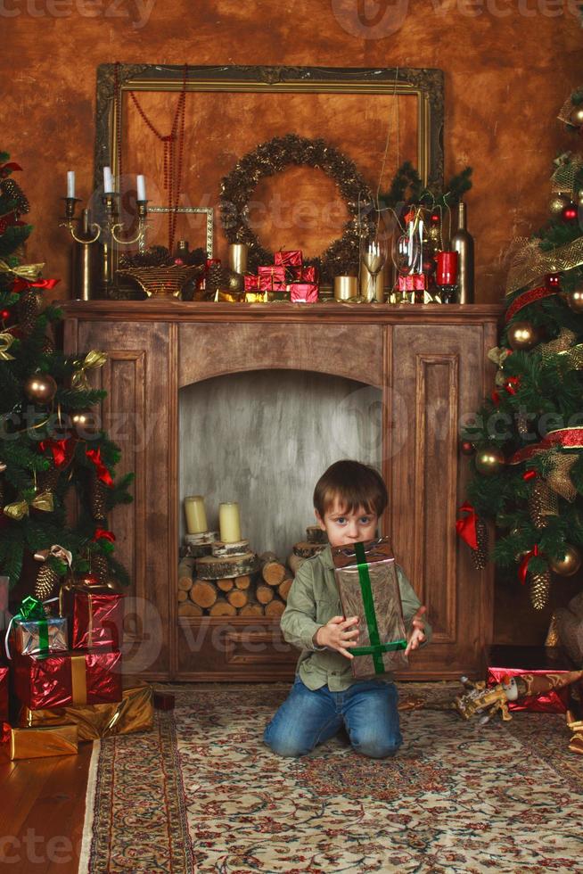 Kind Junge sitzt unter dem Weihnachtsbaum mit Geschenkbox foto