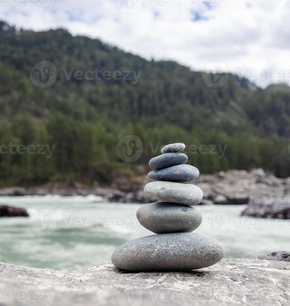 eine Pyramide aus nackten Steinen, die übereinander gestapelt sind. Steine, die in Form einer Pyramide am Flussufer vor dem Hintergrund der Berge gestapelt sind, als Gleichgewicht und Gleichgewicht in der Natur, Zen, Buddhismus. foto
