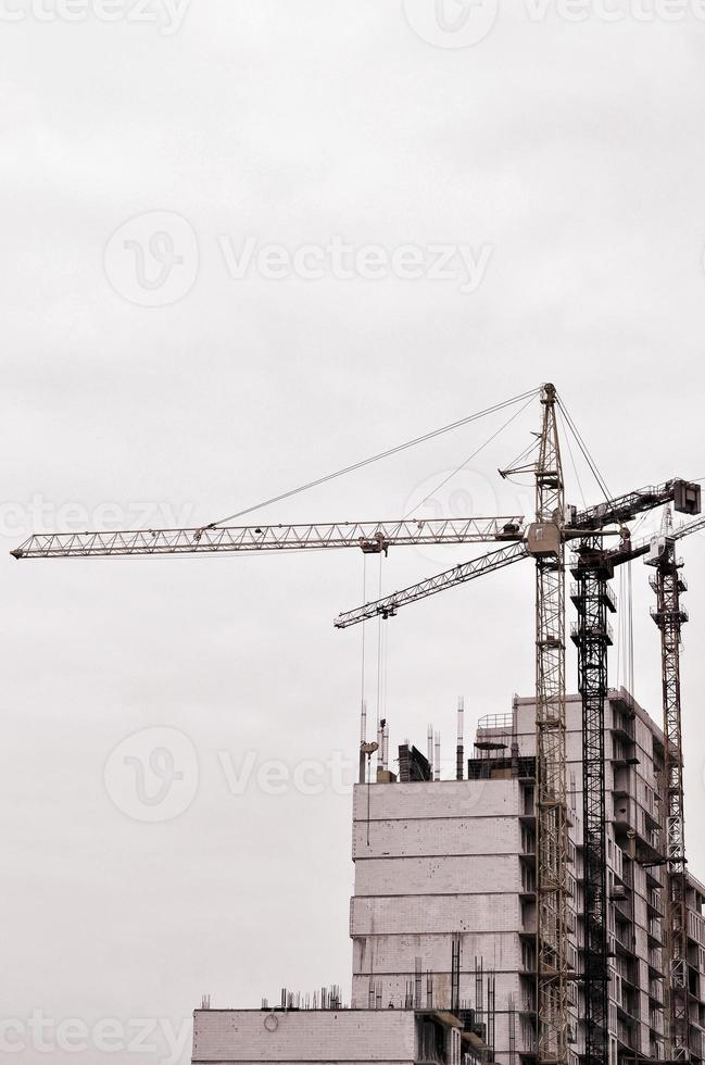 arbeitende hohe Kräne im Inneren mit hohen Gebäuden im Bau vor einem strahlend blauen Himmel. Fortschritt der Kran- und Bauarbeiten. Retro-Ton foto