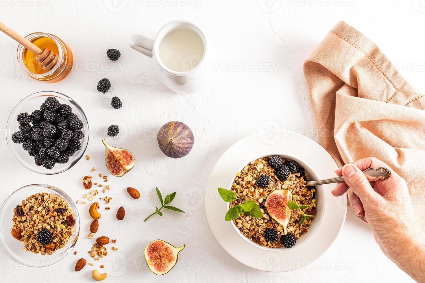 die Hand einer jungen Frau mit einem Löffel Müsli oder Müsli gefüllt während des Frühstücks. ein Teller Müsli, Brombeeren und eine Feigenscheibe. Ansicht von oben. foto