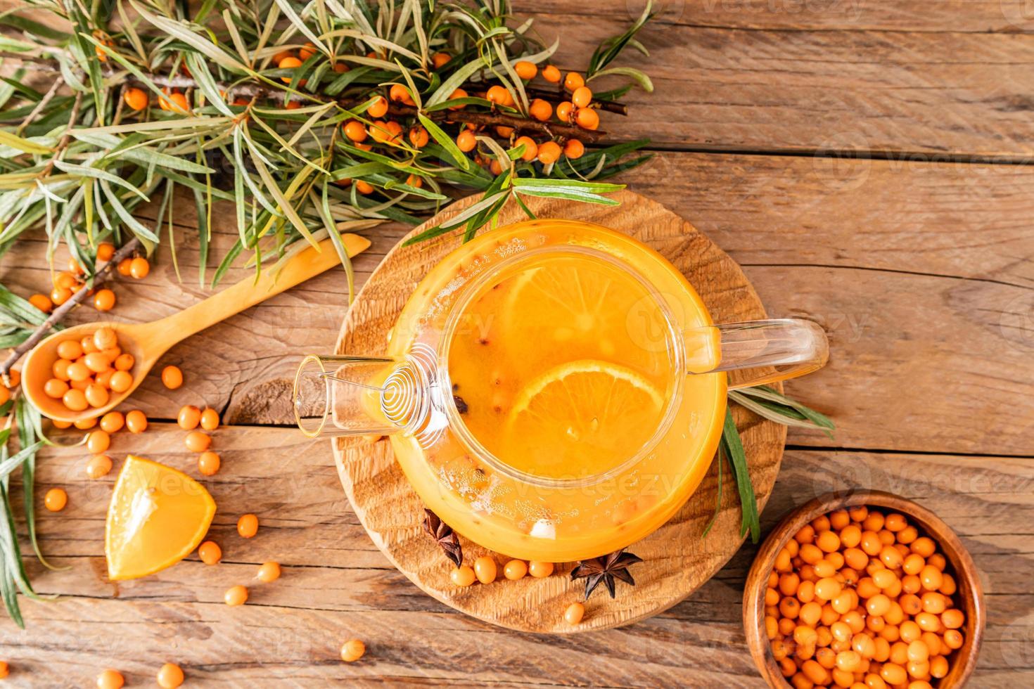 heißer Vitamin-Sanddorn-Tee in eine Teekanne aus Glas, steht auf einem alten Holzhintergrund. entspannung und kräutermedizin, erkältungsgetränk, grippesaison foto