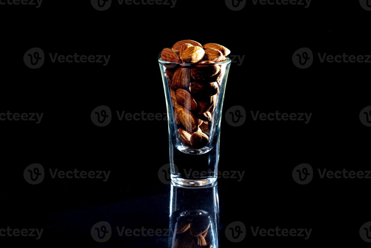 geschälte Mandeln im Weinglas-Eimer auf schwarzem, isoliertem Hintergrund. Reihe von Schalen mit Mandelnüssen, Vorderansicht. foto