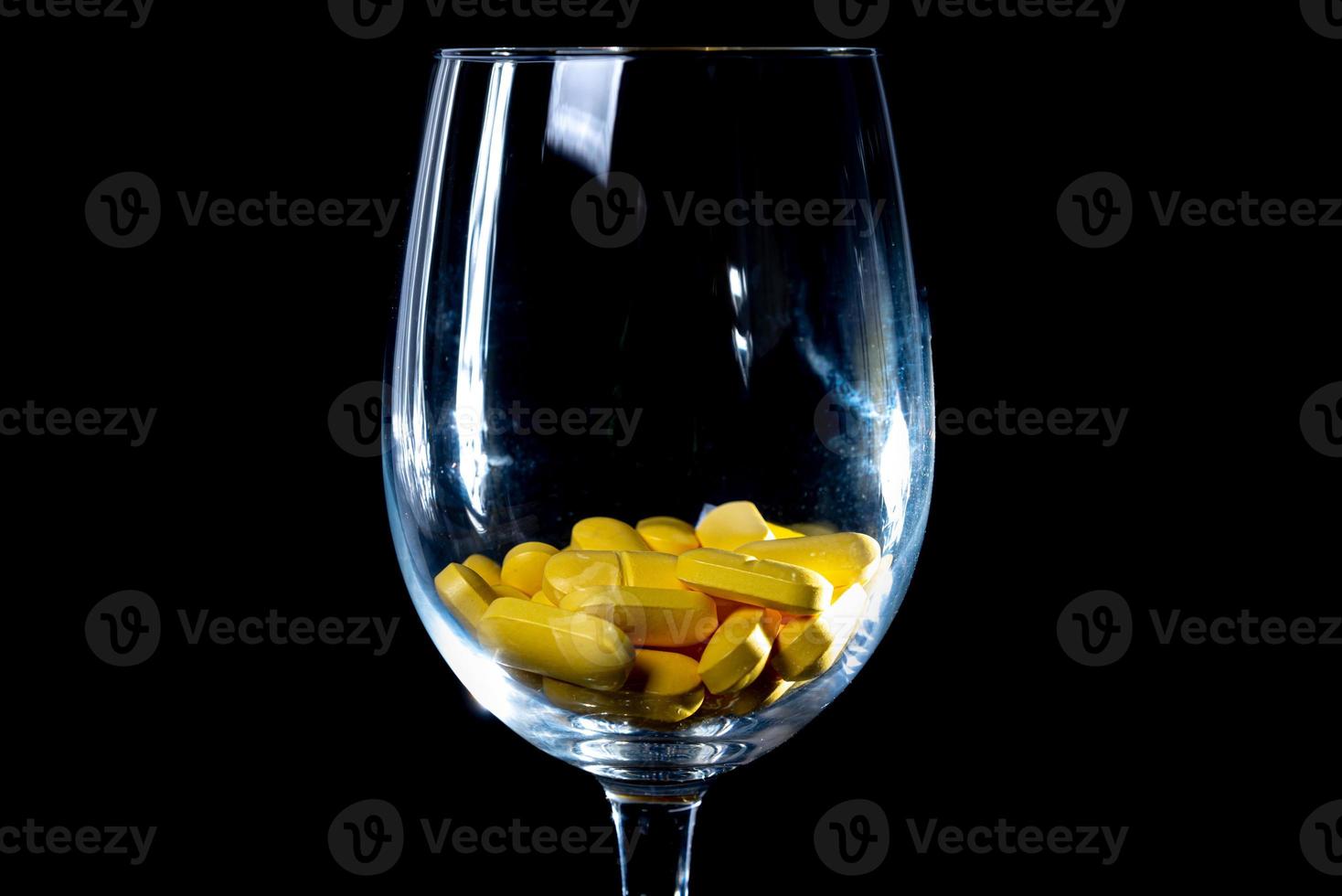 weiße orangefarbene Pillen im Weinglasglas. im Glas. in Eimer isoliert auf schwarzem Satz von Kapseln und Pillen in Nahaufnahme, foto