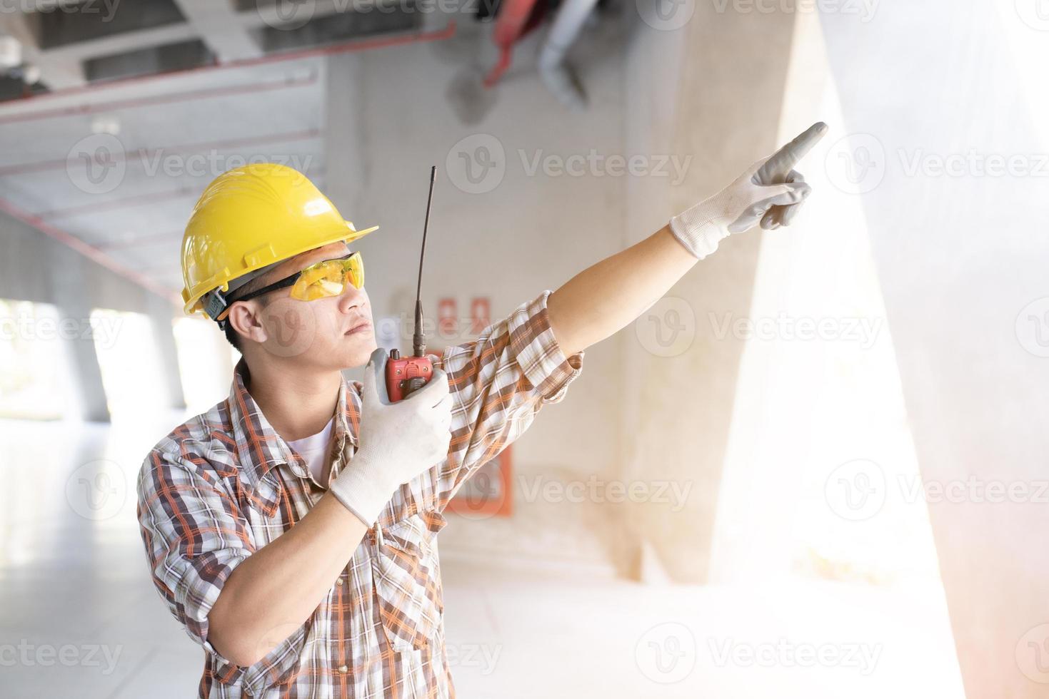 junge arbeiter sprechen über funkkommunikation und tragen einen helmpflanzenhintergrund, nahaufnahme von ingenieuren, die auf einer baustelle arbeiten. foto