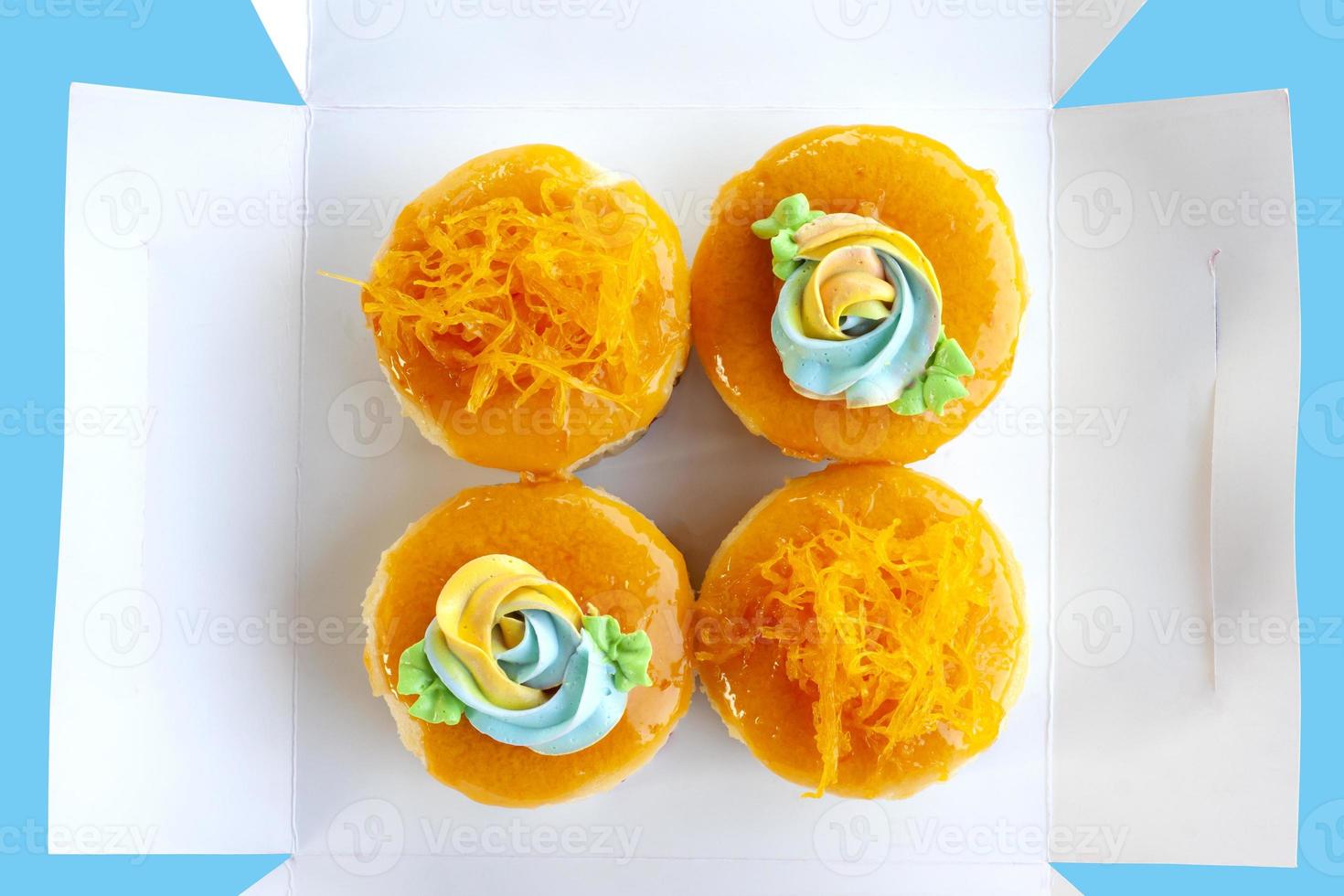 Blick von oben auf Cupcakes im thailändischen Stil und goldene Eigelb-Thread-Kuchen in einer offenen weißen Papierbox, die auf blauem Hintergrund isoliert ist. foto