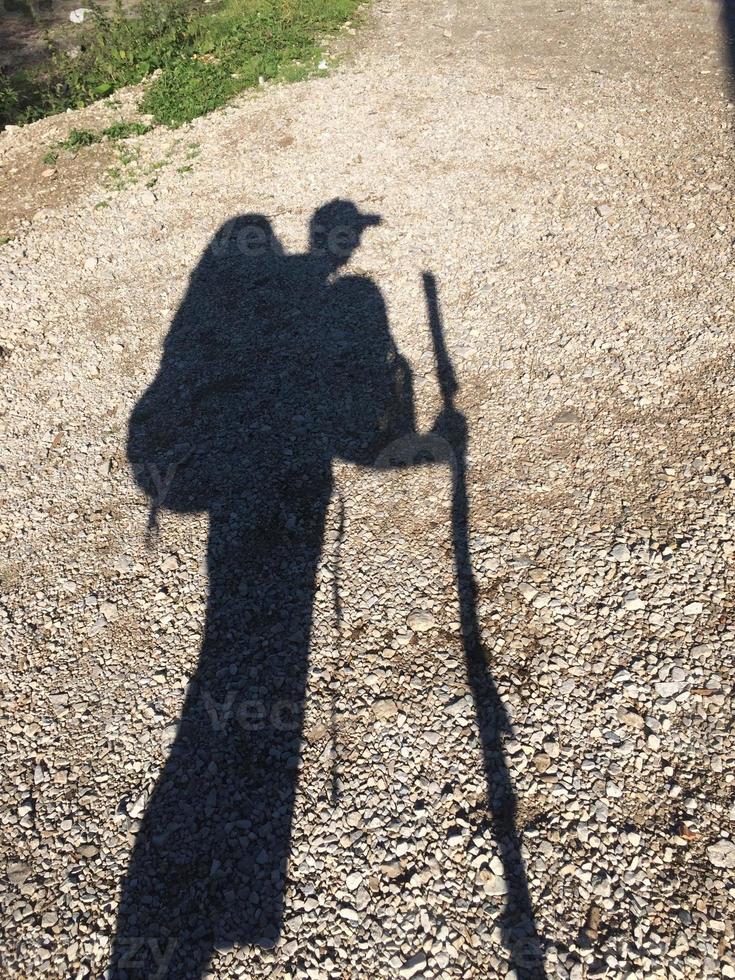 Schatten eines Wanderers mit mehreren Rucksäcken und Wanderstock foto