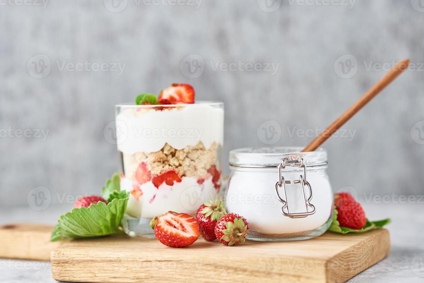 Müsli oder Joghurt mit Erdbeeren im Glas, frische Beeren und Glas mit Zucker foto