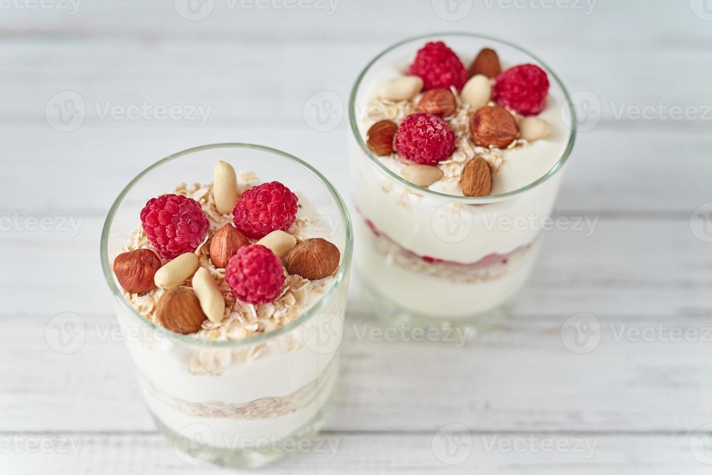 zwei Gläser griechisches Joghurt-Müsli mit Himbeeren, Haferflocken und Nüssen foto