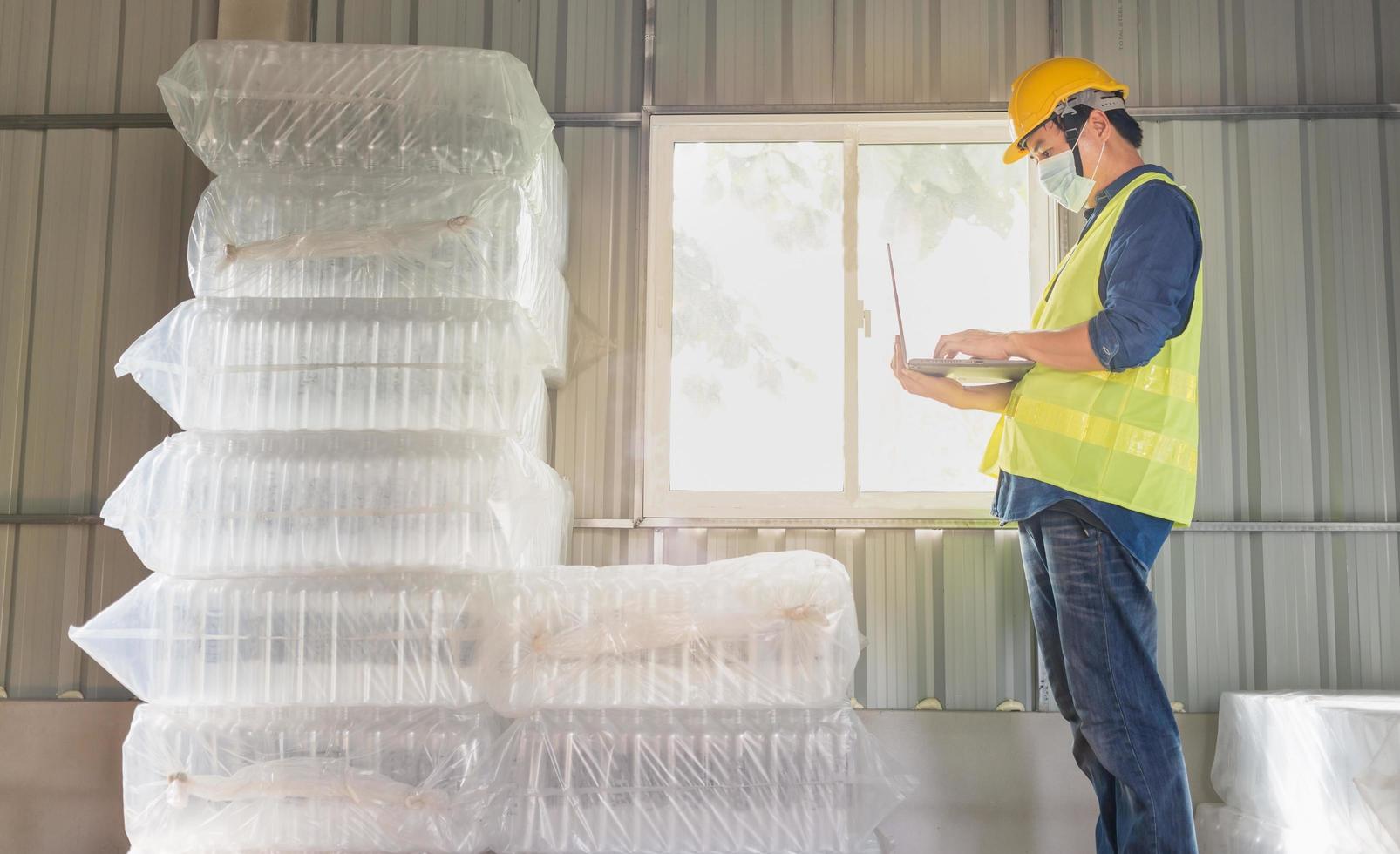 Junger Arbeiter und Qualitätsprüfer in einer Fabrik, die die Anzahl der weißen Plastikflaschen im Lager überprüft foto