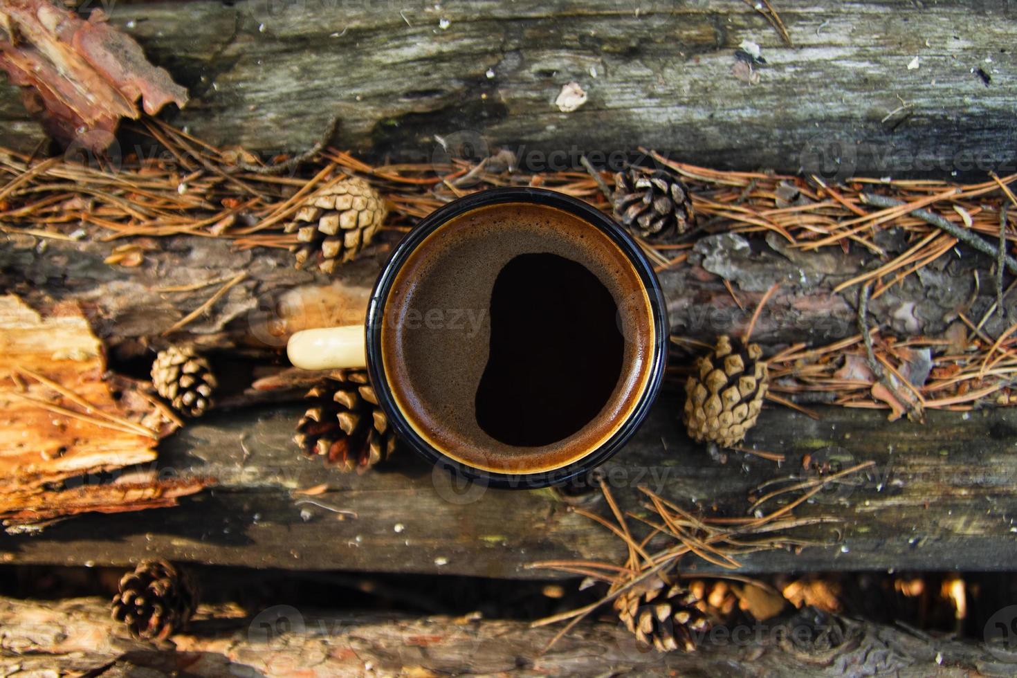 Gelbe Metalltasse mit heißem Kaffee auf dem Holzhintergrund mit Münzen, Nadeln und Baumrinde, Draufsicht. foto