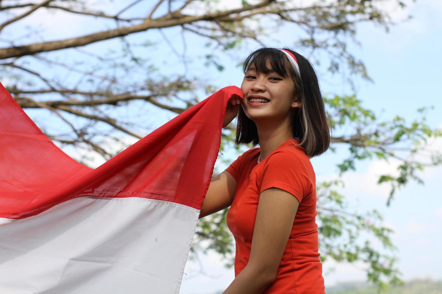 schöne junge asiatin, die die indonesische flagge mit einem fröhlichen gesicht trägt foto