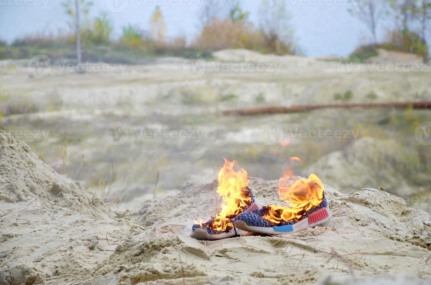 brennende sportschuhe oder turnschuhe in feuer stehen an der sandstrandküste. Sportler ausgebrannt. körperliche anstrengung während des trainingskonzepts foto