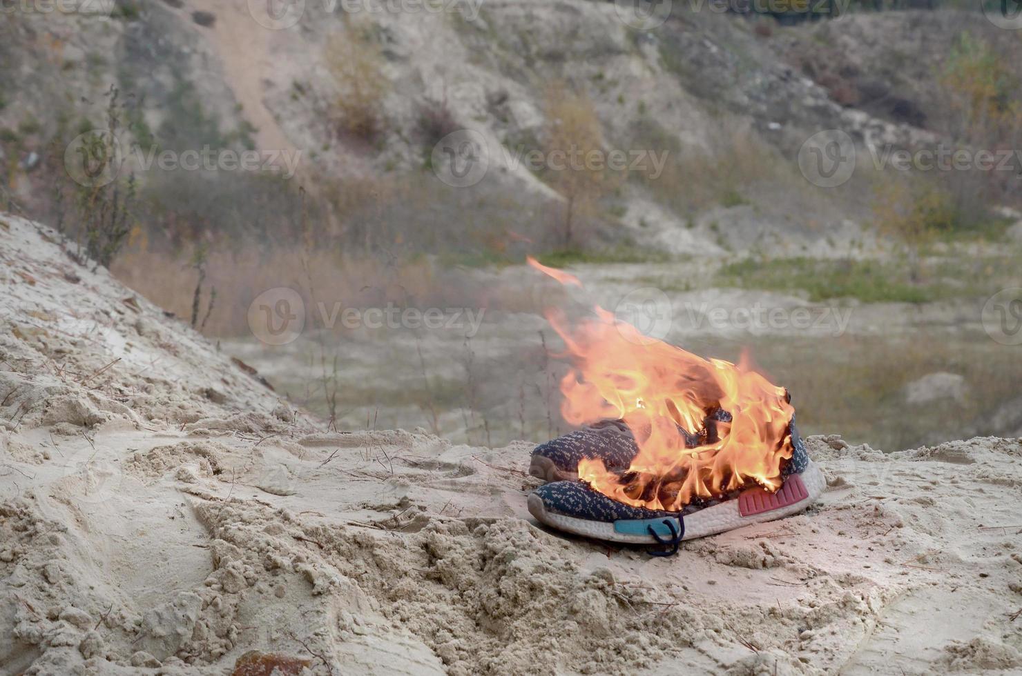 brennende sportschuhe oder turnschuhe in feuer stehen an der sandstrandküste. Sportler ausgebrannt. körperliche anstrengung während des trainingskonzepts foto