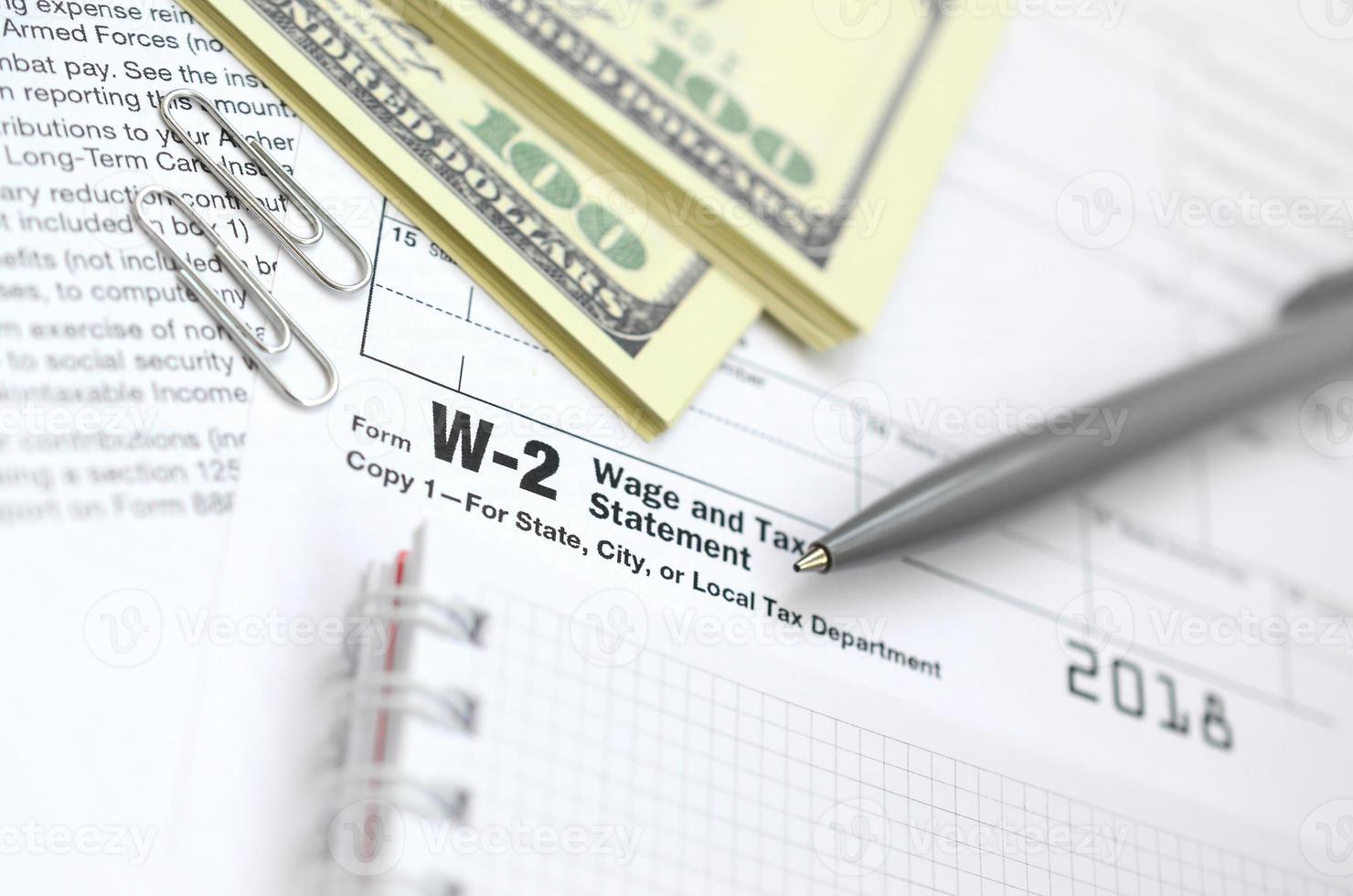 der stift, notizbuch und dollarschein liegt auf dem steuerformular w-2 lohn- und steuerbescheinigung. die Zeit, Steuern zu zahlen foto