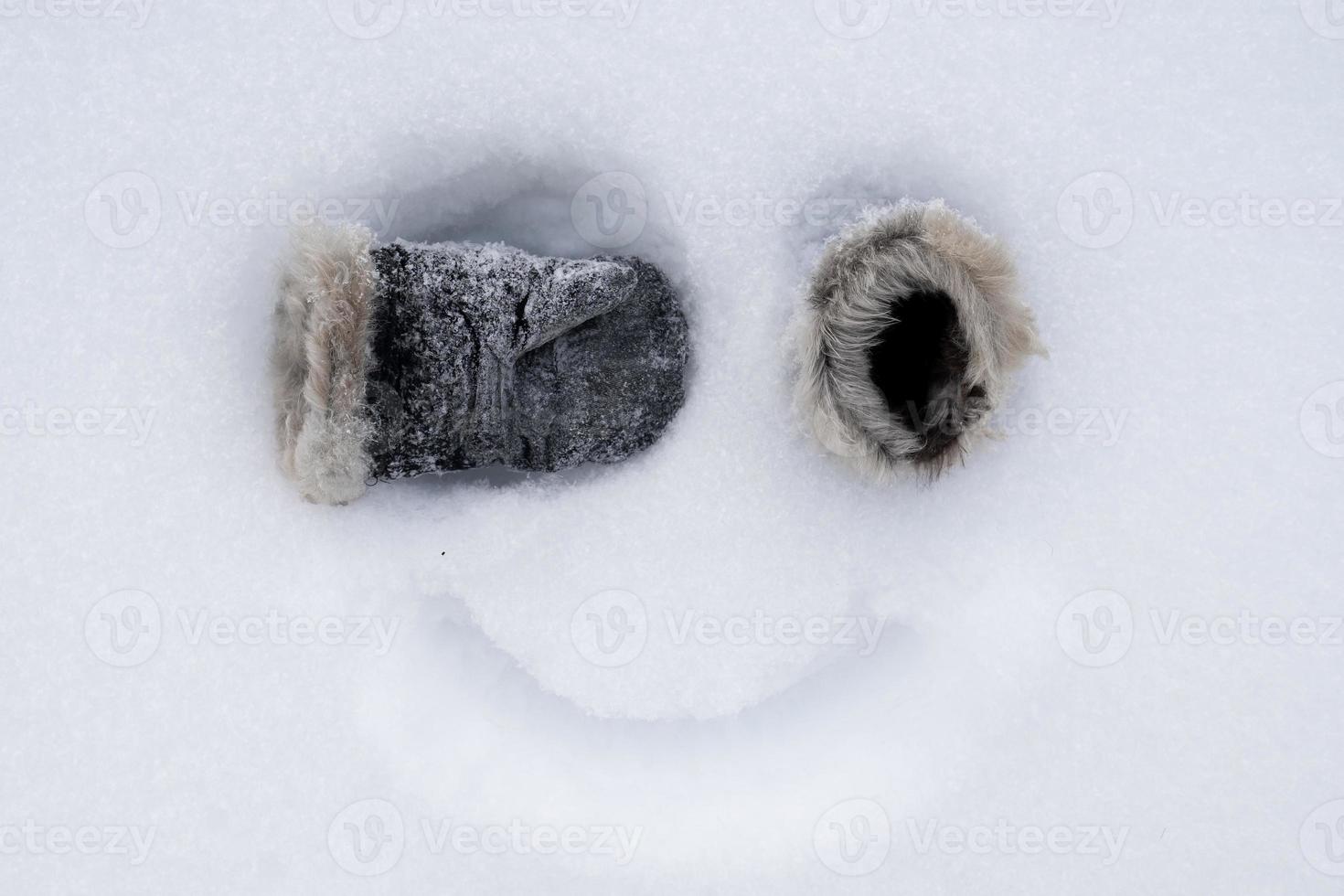 lustiges hausgemachtes Smiley-Gesicht, mit Fäustlingen statt Augen und einem gemalten Lächeln auf dem Schnee. kreative Idee. Ansicht von oben. foto