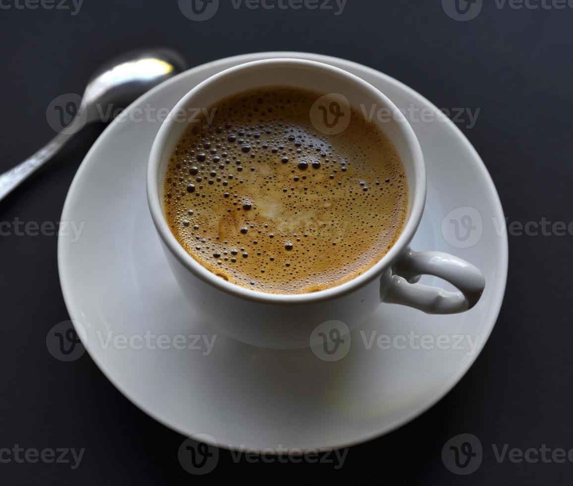 Saftiger frisch gebrühter Kaffee mit Schaum in einer weißen Tasse auf schwarzem Hintergrund. schöne tasse kaffee nahaufnahme von oben. foto