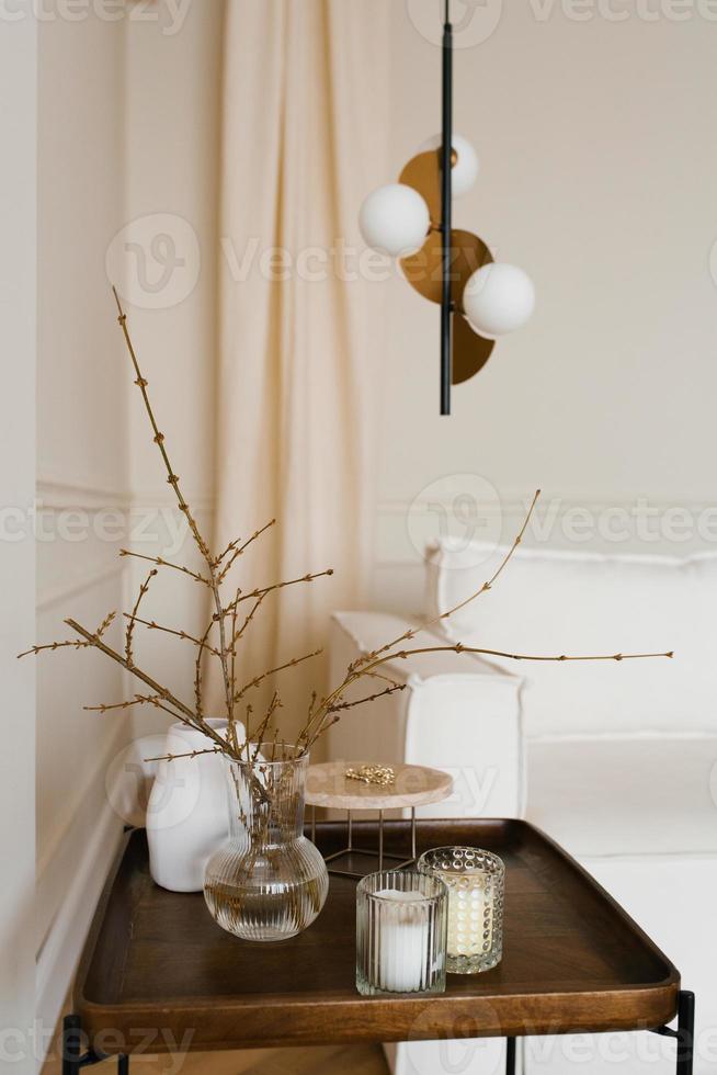 Baumzweige mit eingeführten Knospen in einer Glasvase und Kerzen auf einem hölzernen Couchtisch. Skandinavische Wohnzimmerdekoration foto