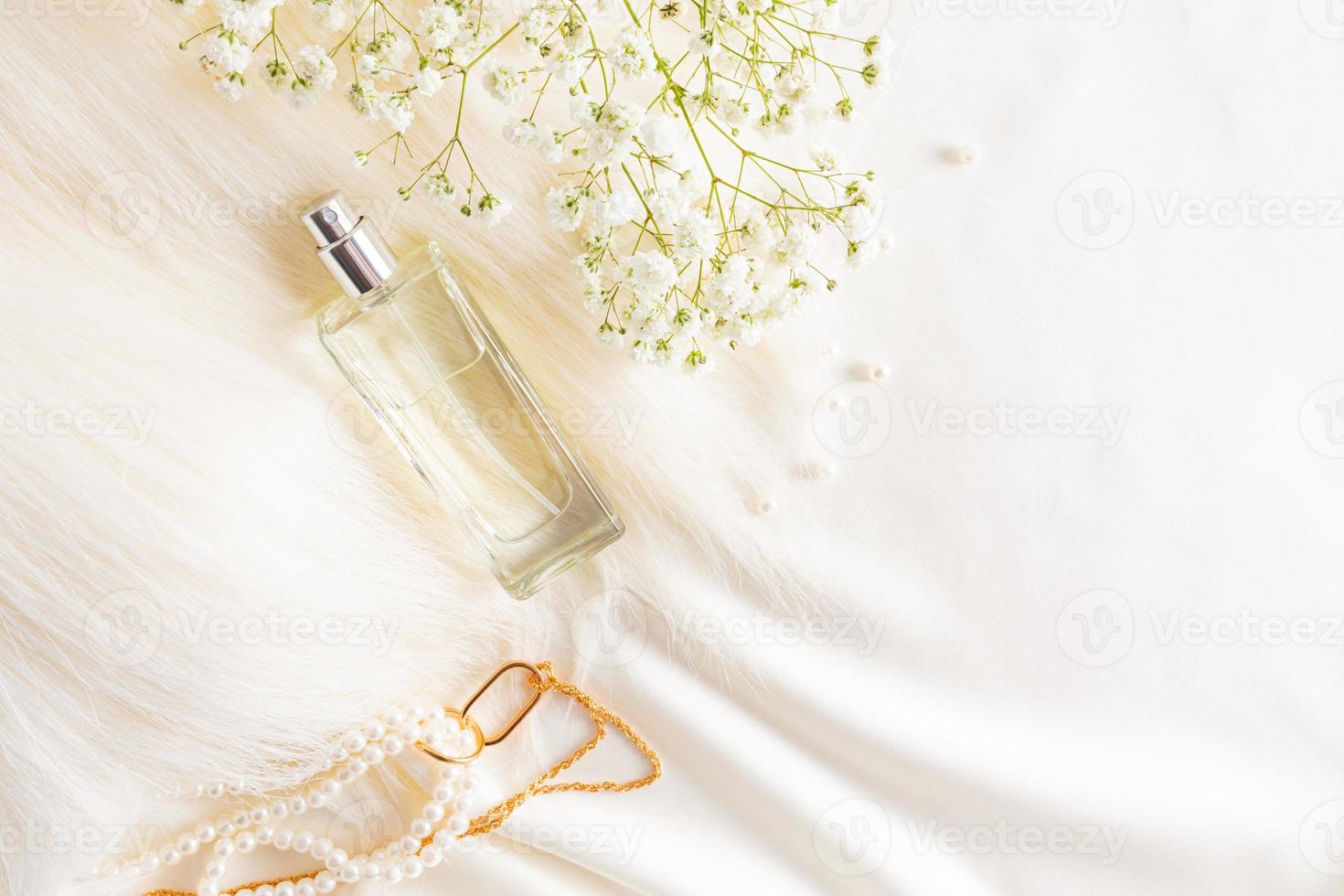 Draufsicht auf eine schicke Flasche Damenparfüm auf einem pastellfarbenen Satinstoffhintergrund mit Perlen und einem Gypsophila-Zweig. Werbekonzept. foto