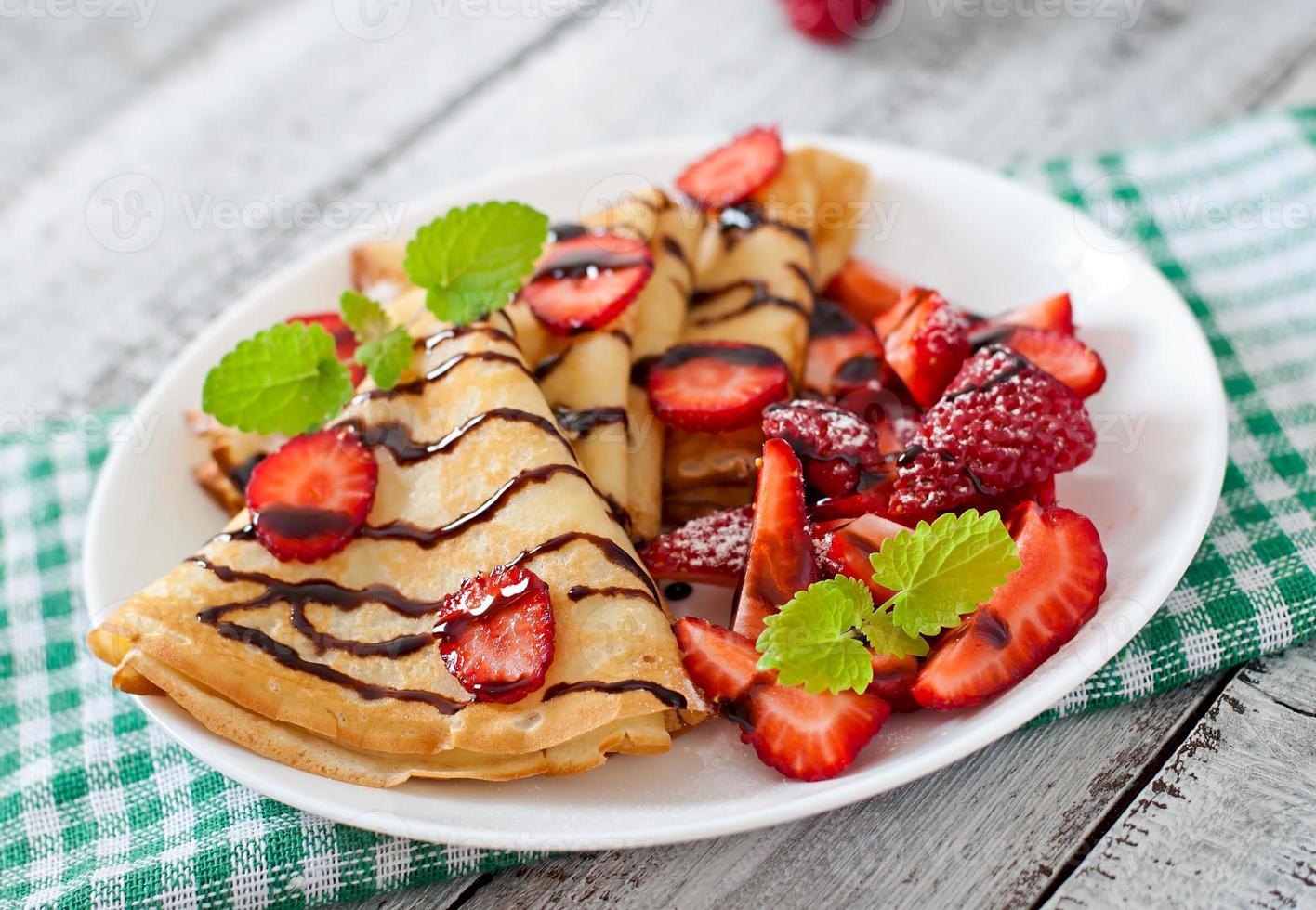 Pfannkuchen mit Erdbeeren und Schokolade, verziert mit Minzblatt foto