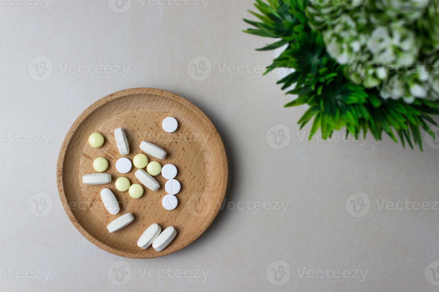 Eine Handvoll Pillen in einem Holzteller mit grüner Pflanze. das konzept der medizin, behandlung. Ansicht von oben. foto