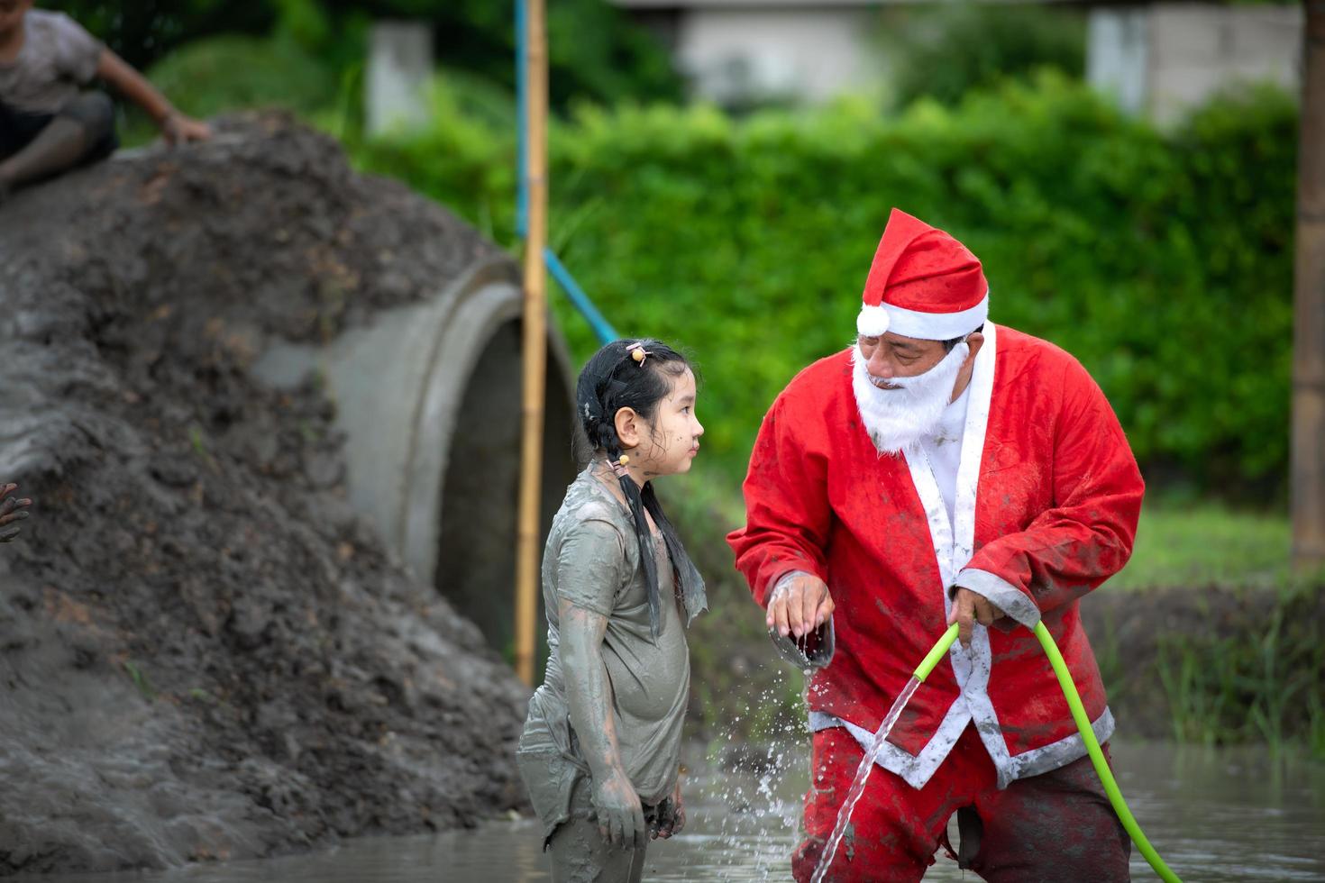 Der freundliche Weihnachtsmann hilft dabei, den Schlamm abzuwaschen, der auf Gesicht und Augen der Kinder gelangt foto
