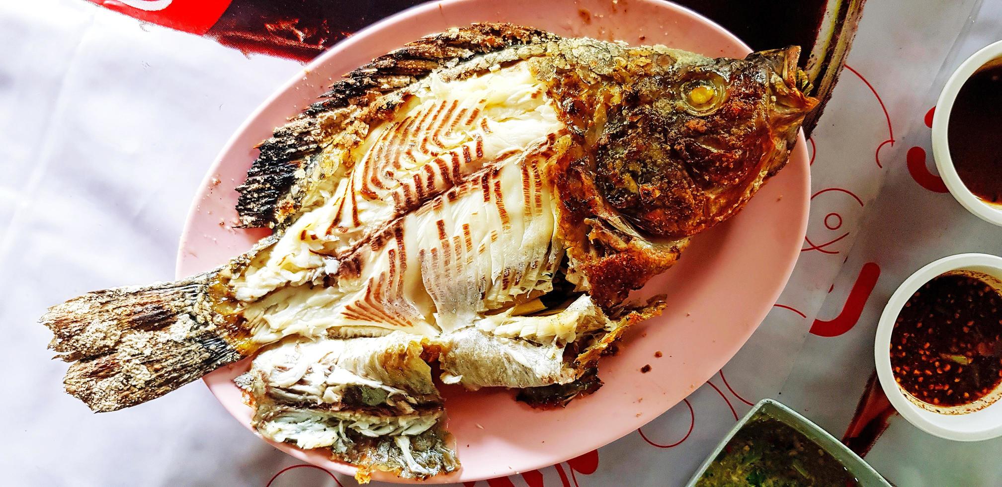 Draufsicht auf thailändischen gegrillten Tilapia, Karpfen oder Granatapfelfisch auf rosafarbenem Teller oder Gericht mit würziger und süßer Sauce im lokalen Streetfood-Restaurant. gesunde ernährung und diätkost. foto