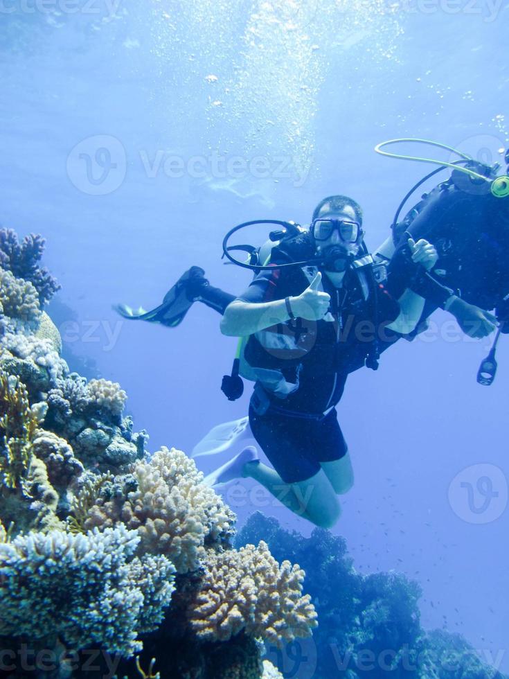 eine schöne taucherin zeigt hände gesten signal alles gut mit einem partnerausbilder für sicherheitsschwimmer unter wasser im roten meer mit korallenriffen ägypten, sharm el-sheikh foto