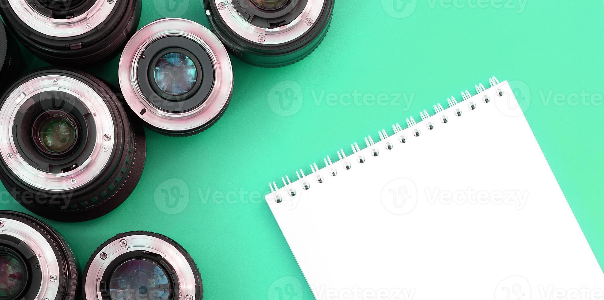 Mehrere Fotoobjektive und ein weißes Notizbuch liegen auf einem helltürkisfarbenen Hintergrund. Platz kopieren foto