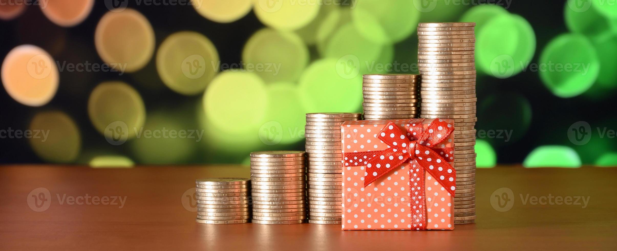 Kleine rote Geschenkbox und goldene Münzstapel auf dem farbigen Bokeh-Hintergrund foto