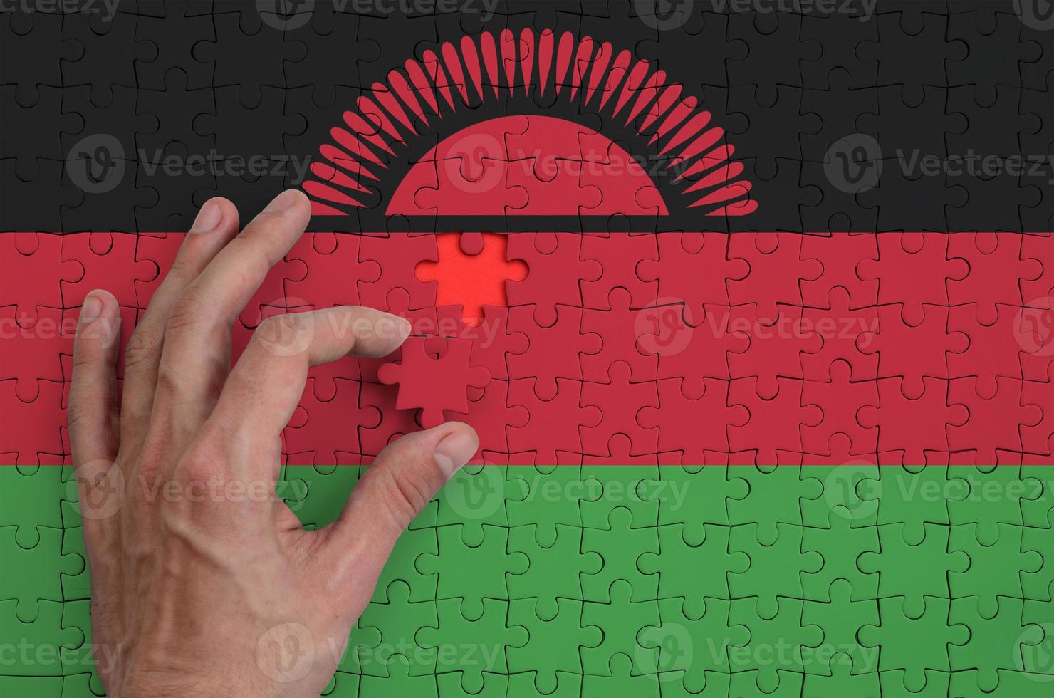 Die Malawi-Flagge ist auf einem Puzzle abgebildet, das die Hand des Mannes zum Falten vervollständigt foto