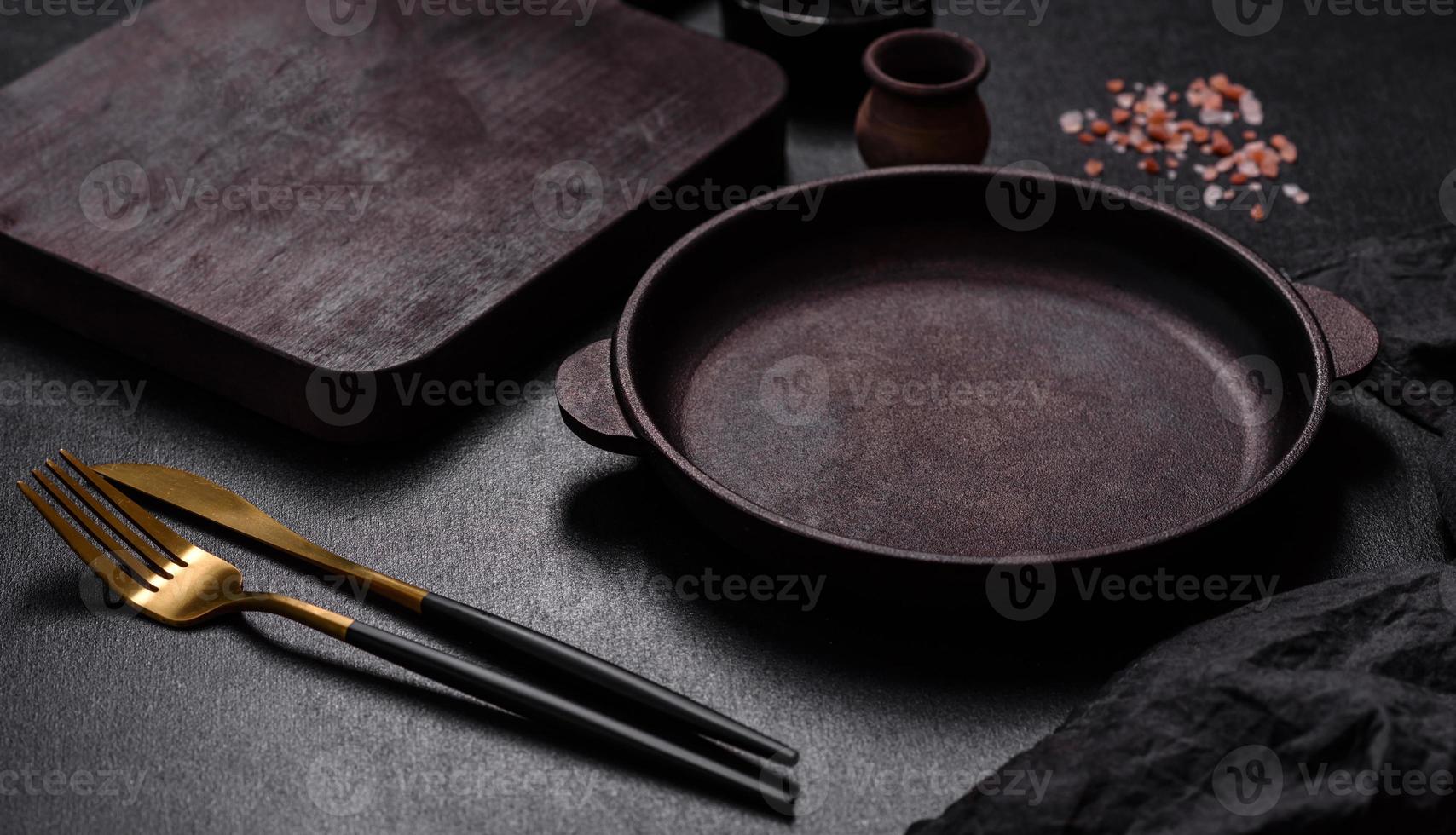 Braune Eisenpfanne mit Küchenutensilien auf dunklem Betongrund foto
