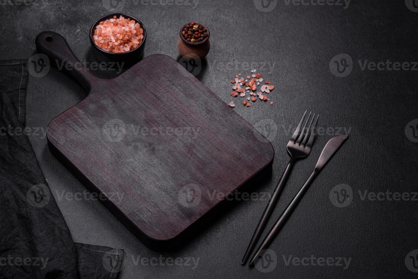 Holzschneidebrett mit Küchengeräten auf schwarzem Betongrund foto