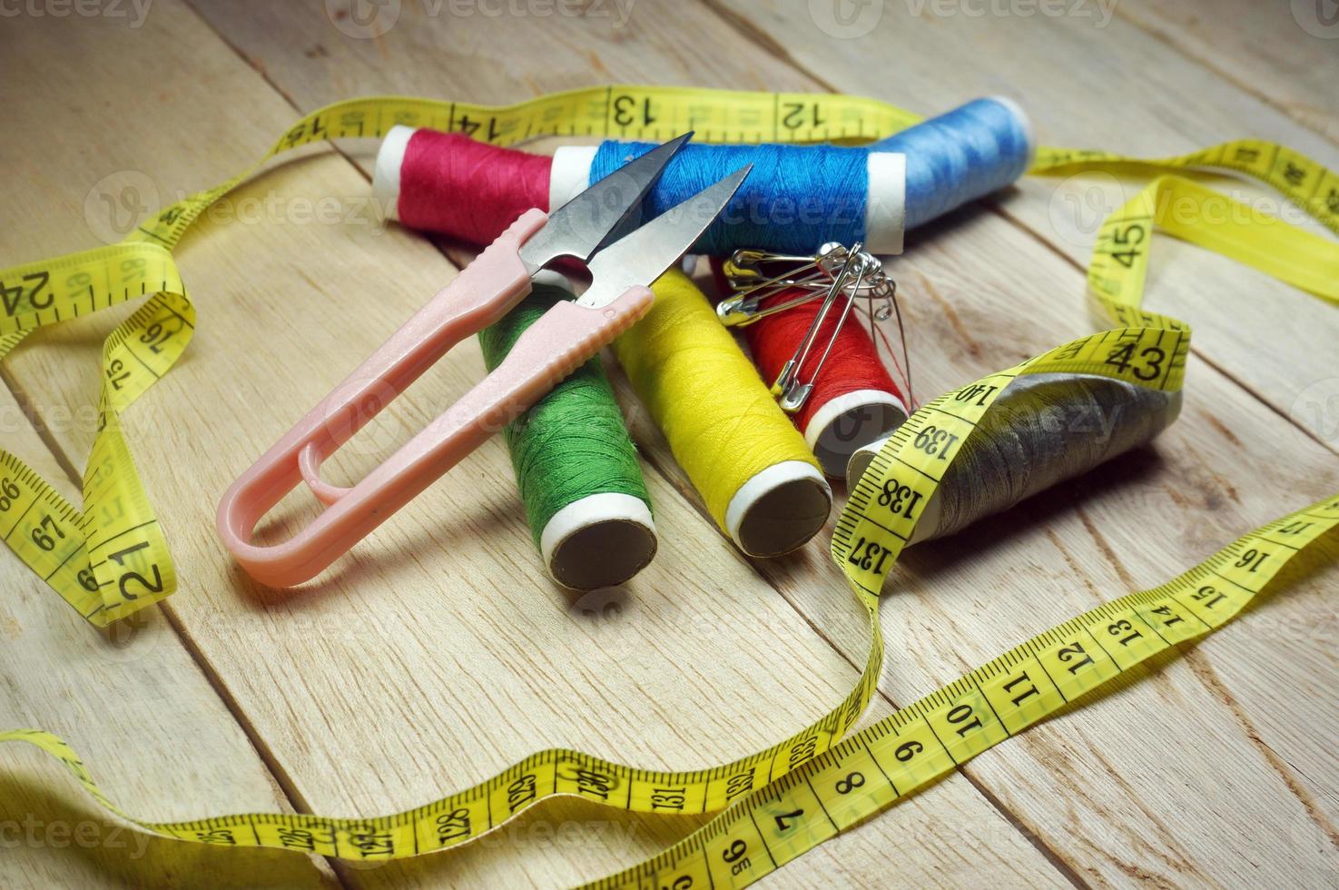 Garnrollen und grundlegende Nähwerkzeuge wie Stifte, Nadel, Fingerhut, Maßband und Garnschere auf einem Holztisch foto
