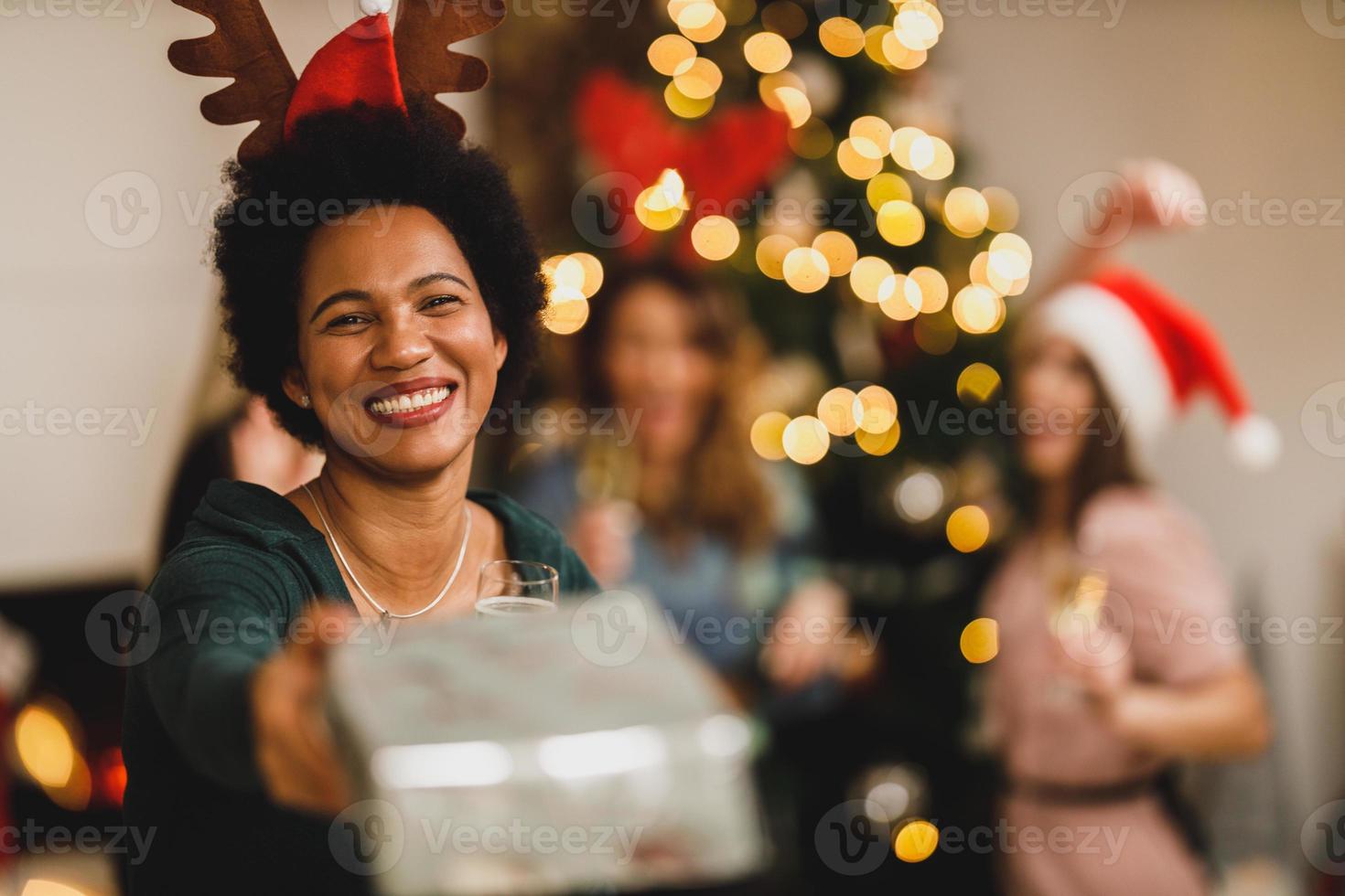 afrikanisch-amerikanische frau, die geschenke gibt, während sie sich zu hause versammelt hat, um weihnachten oder neujahr mit freunden zu feiern foto