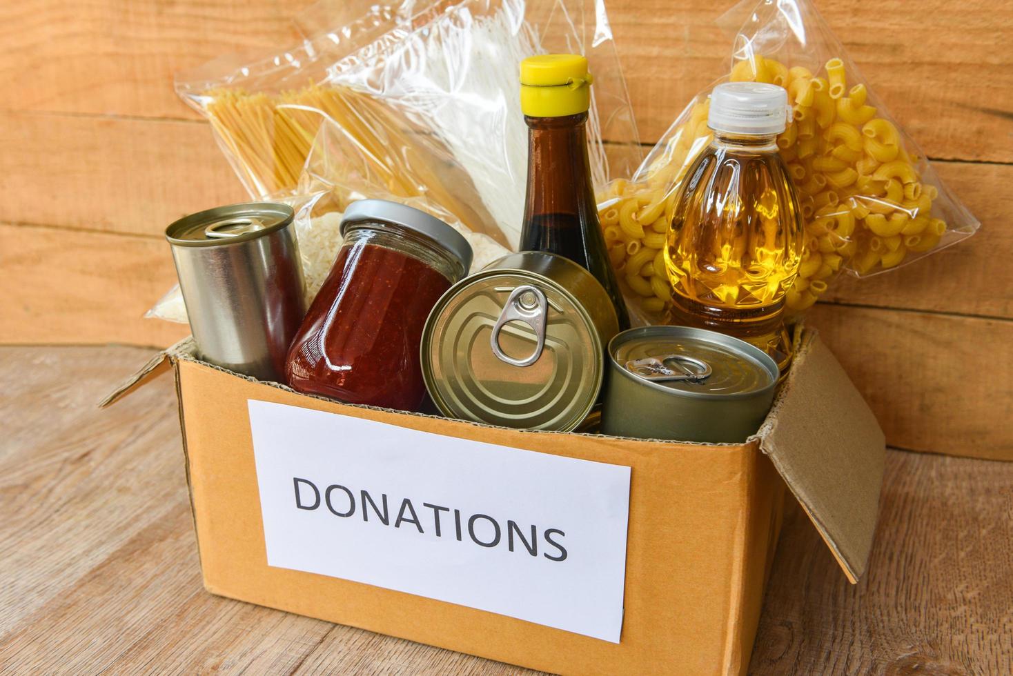 Spendenbox mit Konserven auf Holztisch Hintergrund Pasta Konserven und Trockenfutter nicht verderblich mit Speiseöl Reisnudeln Spaghetti Makkaroni Spenden Lebensmittel foto