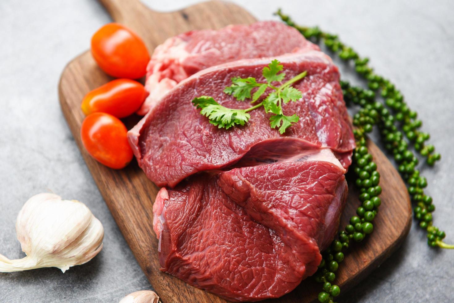 rohes Rindfleisch auf Holzbrett auf dem Küchentisch zum Kochen von Rindersteak gebraten oder gegrillt mit Zutaten Kräuter und Gewürze frisches Rindfleisch tierisches Protein foto
