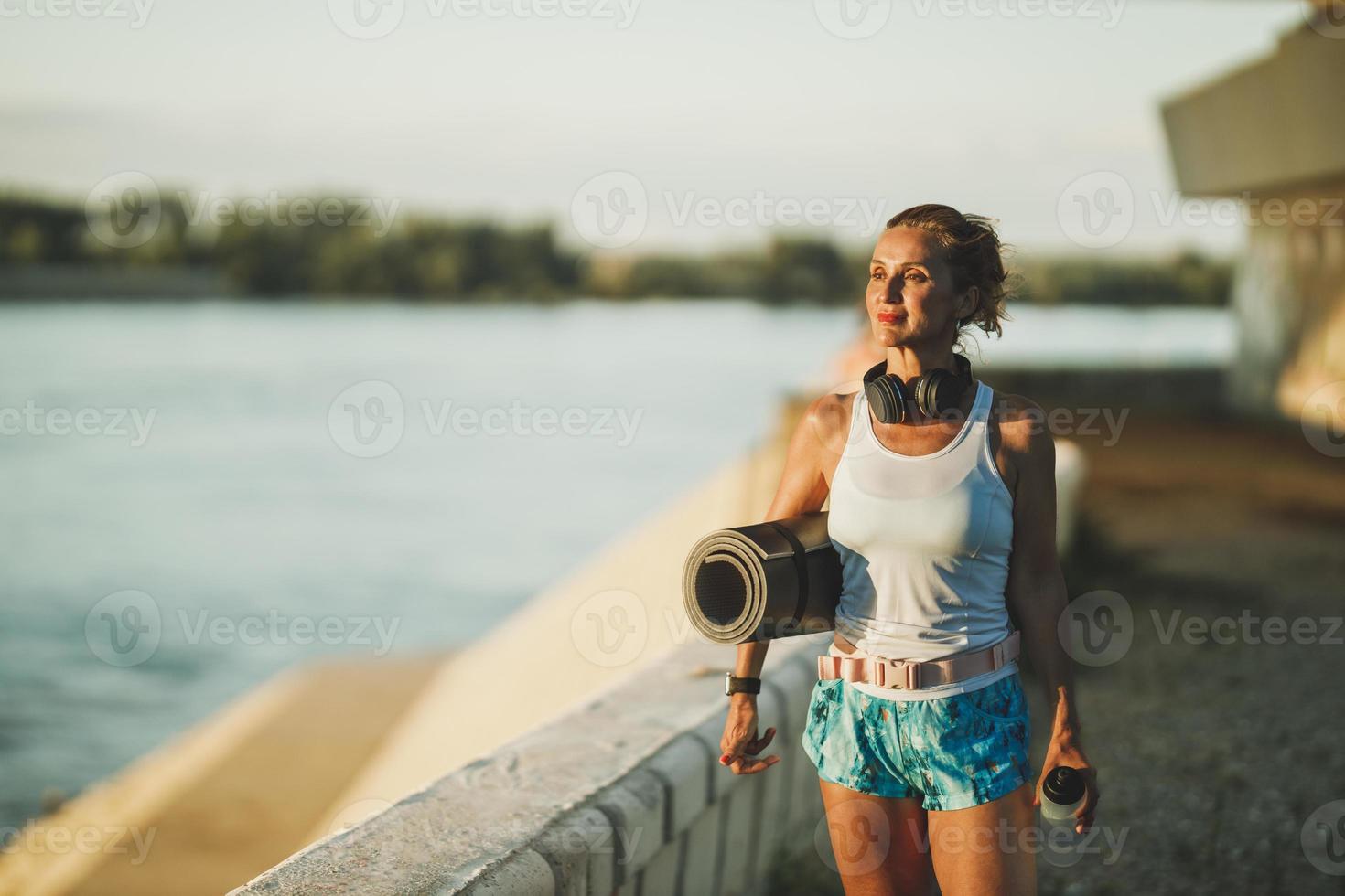 Frau mit aufgerollter Gymnastikmatte und Wasserflasche foto